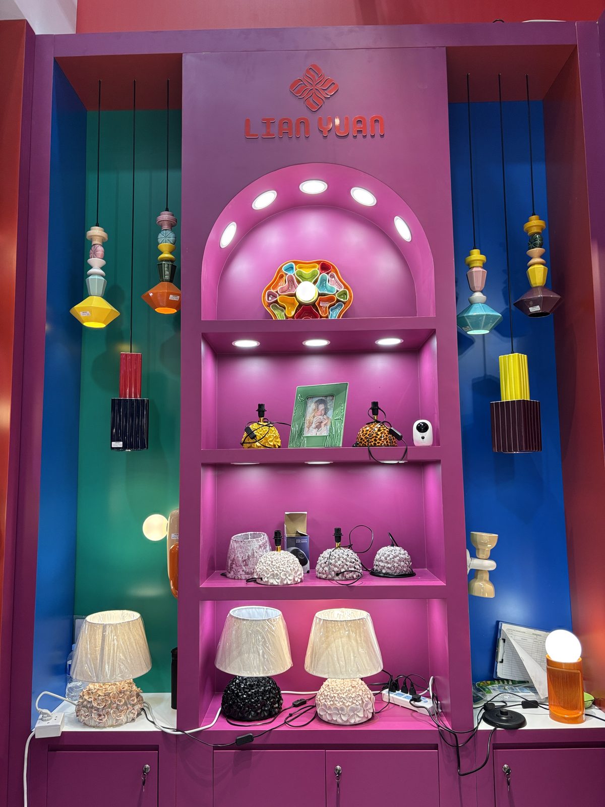 LianYuan stand wall in magenta, teal and blue with pendant lamps, table lamps and decor on lit shelves