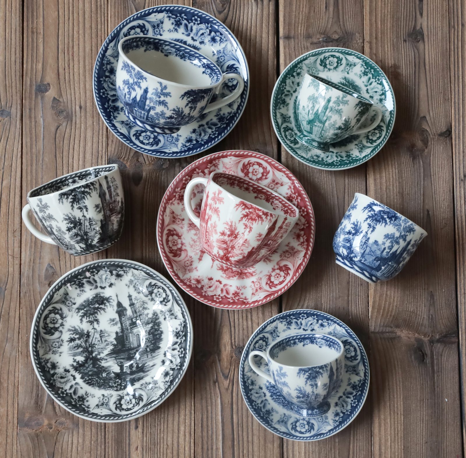 Transferware toile cups and plates in blue, black, red and green on a wooden table